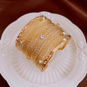 Close-up of golden multi-layer textured cuff bracelet with diamonds on white ceramic