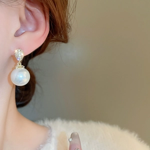 Close-up of elegant gold-plated pearl drop earrings with sparkling zircon on a model