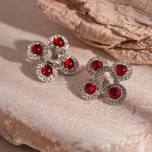 Detailed macro view of silver G-letter stud earrings with red resin and crystals