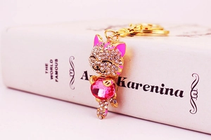 Detailed view of the sparkling rhinestone cat keychain with a pink crystal on a white book