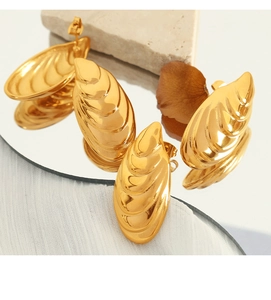 Artistic close-up of golden shell textured earrings reflected on a mirror with flowers