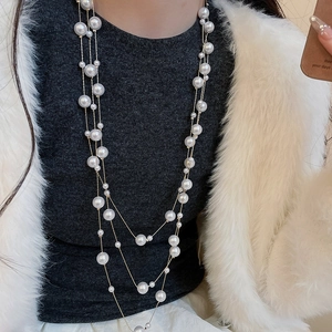 Close-up of layered pearl necklace with gold chains worn over a grey knit sweater