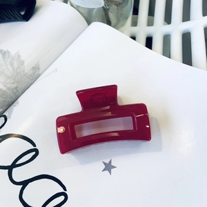 Close-up of a glossy red rectangular hair claw clip resting on a white decorative book