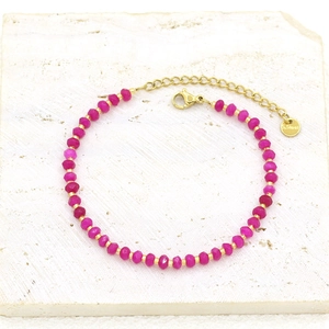Detail of rose red faceted beads and gold-plated stainless steel clasp on a stone surface