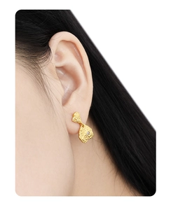 Detail of irregular lava texture gold earring with small diamond on female model ear