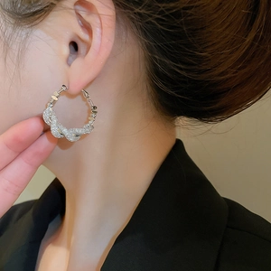Close-up of elegant silver twisted hoop earring with sparkling zircons worn by a model