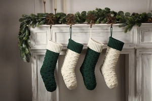 Detail of knitted Christmas stockings in fish-scale pattern hanging on white fireplace