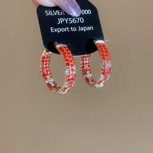 Macro shot of gold hoop earrings with orange and clear crystals on a black display card