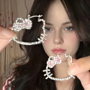 Detailed view of silver Hello Kitty earrings with pink crystal bows on a hand
