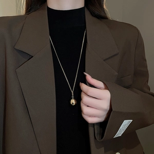 Model wearing gold spherical pendant necklace with delicate chain over a brown blazer