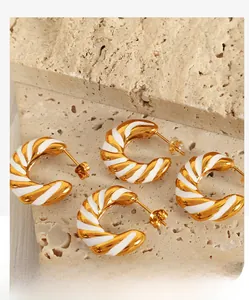 Detailed close-up of gold and white enamel croissant hoop earrings on beige stone