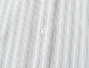 Détail du tissu rayé gris d'une chemise avec bouton blanc et coutures de précision