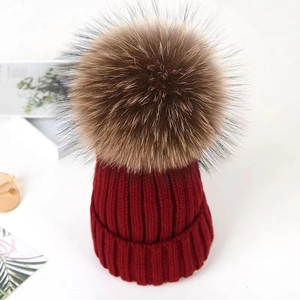 Close-up of deep red knit beanie texture and fluffy large brown faux fur pompom ball