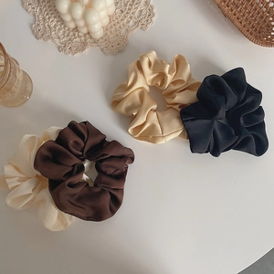 Close-up of assorted satin scrunchies in cream and black on a minimalist white desk