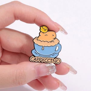Spilla smaltata capybara Cappyccino con pulcino in tazza blu tenuta con le dita