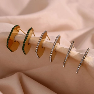 Macro shot of gold-plated stud earrings with green zircon and pearls on pink silk fabric