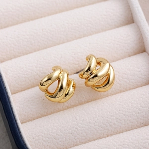 Close-up of 18K gold hollow knot earrings on a beige velvet jewelry box background