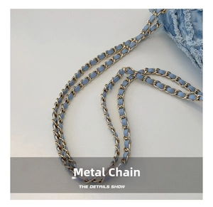 Macro view of gold-tone metal chain with blue denim strap and fringe fabric detail
