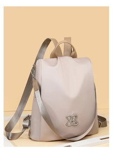 Detail view of beige waterproof nylon backpack featuring elegant silver metal logo ornament