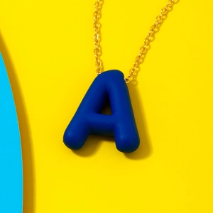 Minimalist golden chain necklace featuring a glossy deep blue letter A pendant on yellow background
