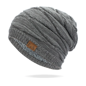 Detail of grey knitted beanie with thick faux fur lining and a brown leather logo tag