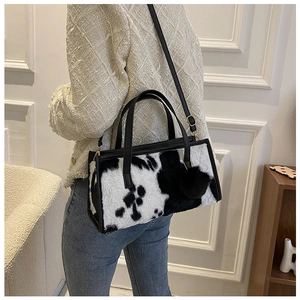 Chic black and white cow print plush handbag with black fuzzy charm and shoulder strap