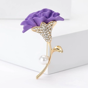 Detailed view of a purple carnation brooch with gold leaves, crystals, and a pearl accent