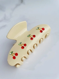 Detail of cream acetate hair claw clip with red rhinestone cherry patterns and accents