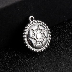 Polished stainless steel round sun pendant with beaded edge on a dark textured surface
