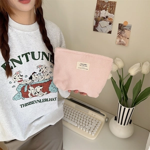 Pink corduroy makeup bag with woven label detail held by model in cozy lifestyle setting