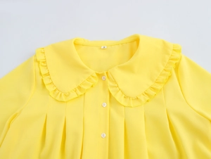 Detail view of yellow Peter Pan collar shirt with ruffle edges and pleated bodice design