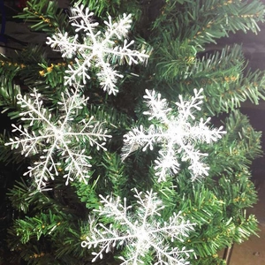White plastic snowflake ornaments with fuzzy texture hanging on a green Christmas tree