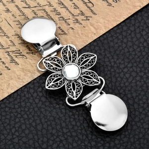 Macro shot of a silver vintage flower cardigan clip with crystal on black leather background