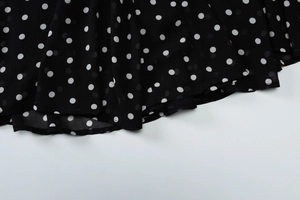 Detailed macro view of black chiffon fabric with white polka dots and elegant flowing pleats