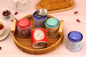 Detail view of round tin tea canisters with vintage rabbit illustrations on a wicker tray