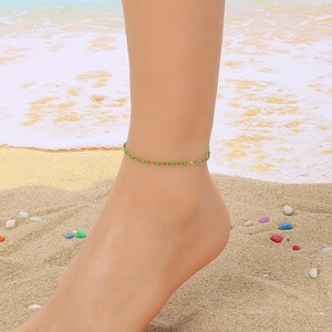 Close-up of golden anklet with green beads on beach sand with soft ocean waves