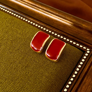 Macro shot of vintage rectangular gold earrings with deep red enamel on green fabric
