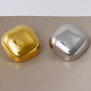 Macro detail of glossy square gold and silver stud earrings on a textured surface