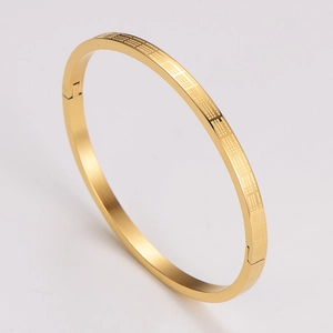 Detail of gold geometric engraved bangle featuring grid patterns and a hinged clasp closure