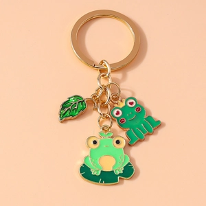 Close-up of green enamel frog and lily pad charms on a golden metal keychain link