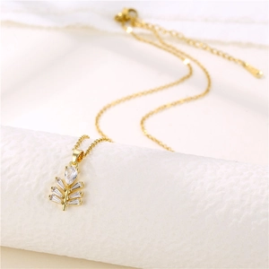 Zircon inlaid leaf pendant necklace in gold-plated titanium steel on white pedestal