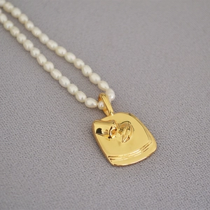 Close-up of elegant freshwater pearl necklace with a gold rectangular embossed coin pendant