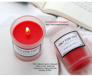 Cozy reading scene with lit red soy wax candle in frosted glass on white fabric