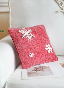 Close-up of red plush Christmas pillow with white snowflake patches on a sofa