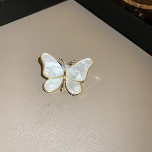 Détail de la broche papillon dorée avec des accents de perles et des ailes irisées