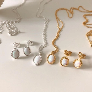 Detailed view of oval opal necklace and stud earring sets in silver and gold finishes