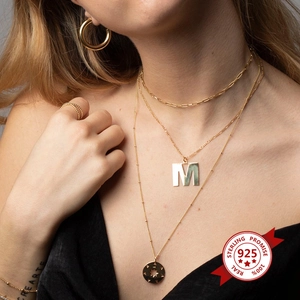 Close-up of layered 925 sterling silver necklaces with M letter and star pendants