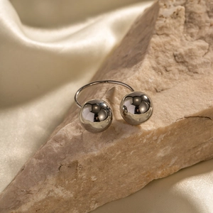 Silver stainless steel open ring with two large spheres placed on a rugged rock
