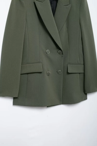 Détail d'un blazer vert à double boutonnage avec revers et poches à rabat sur fond blanc