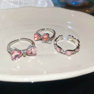 Detailed close-up of three pink crystal heart and bow rings on a white ceramic plate